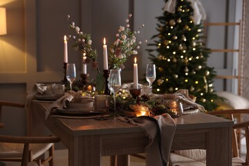 Christmas table setting with stylish dishware, glasses and burning candles in festive decorated room
