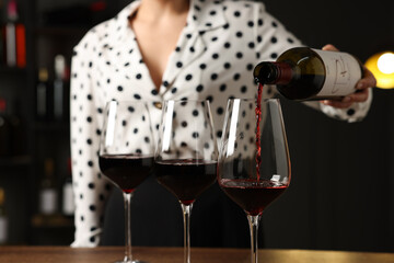 Professional sommelier pouring red wine into glasses at wooden table indoors, closeup