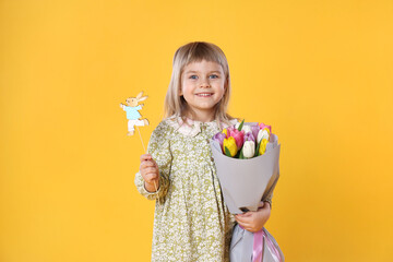 Smiling little girl with bouquet of tulips and decorative Easter bunny on orange background