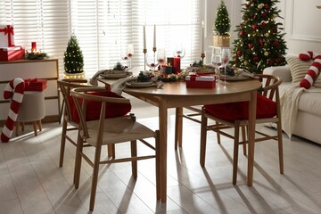 Christmas table setting with stylish dishware, glasses and burning candles in festive decorated room