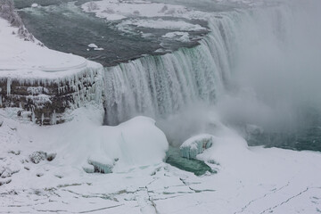 The edge of Niagara Falls with turquoise water from the top next to an icy rock.
