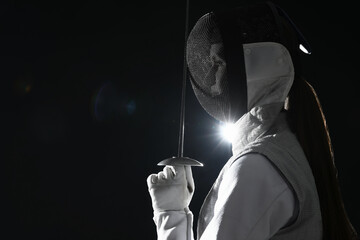 Fencer with epee on dark background, space for text