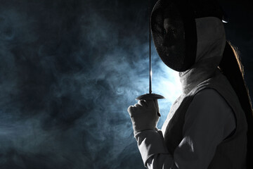 Fencer with epee in smoke on black background, space for text