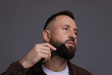 Handsome man combing beard on grey background