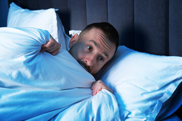 Fear of darkness. Scared man lying on bed in room at night