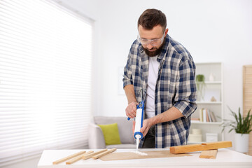 Man with caulking gun glueing plywood indoors