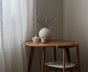 A cozy still life - a round ceramic vase with dry branches, a teapot, a cup on a round wooden table...