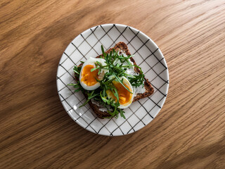 Sandwich with cream cheese, boiled egg, arugula on a wooden background