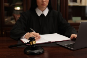 Judge working with laptop at wooden table in office, focus on gavel