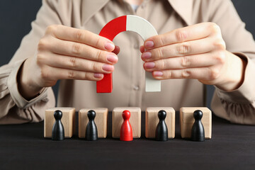 Woman with magnet attracting game pieces at wooden table, closeup