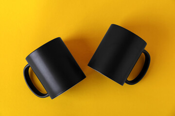 Two blank black mugs on yellow background, top view. Mockup for design