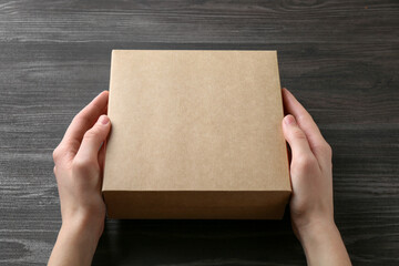 Obraz premium Woman with blank cardboard box on dark wooden background, closeup. Mockup for design