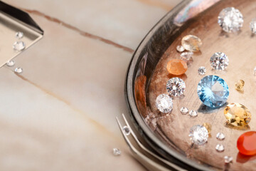 Tray with beautiful gemstones and tweezers on light table, closeup. Space for text