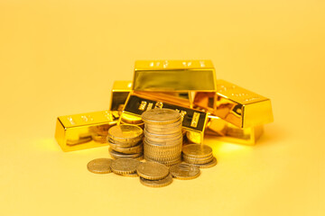 Gold bars and coins on pale yellow background, closeup