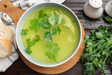 Tasty chicken bouillon in bowl, bread and ingredients on wooden table, flat lay