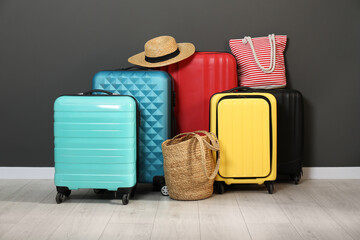 Colorful suitcases, beach bags and hat on floor near black wall