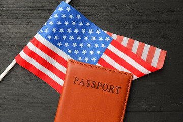 Passport in brown cover and flag of United States on black wooden table, top view