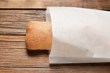 Paper bag with fresh ciabatta on wooden table, closeup