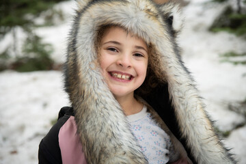 Smiling happy little girl outside in winter wearing warm faux fur hood