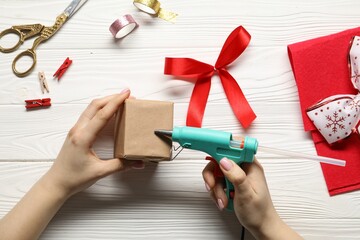 Woman with hot glue gun making craft at white wooden table, top view