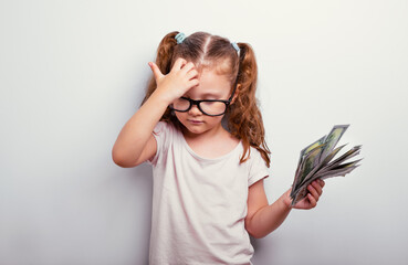 Thinking coach kid girl in eyeglasses holding the money, cash dollars in the hand and scratches her...