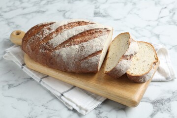 Wooden cutting board and loaf of bread on white marble table