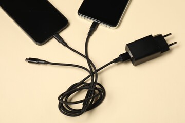 Triple charge cable connected to smartphones on beige background, above view
