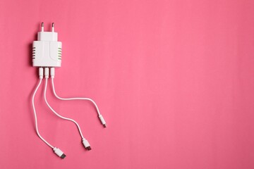 USB power adapter with charge cables on pink background, top view. Space for text