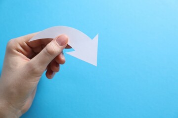 Woman with paper arrow on light blue background, top view. Space for text