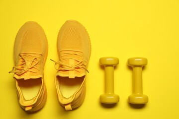 Dumbbells and sneakers on yellow background, flat lay