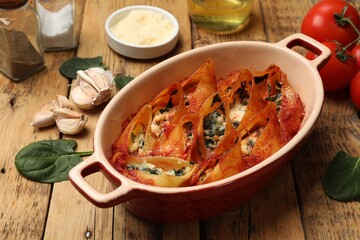 Delicious conchiglie pasta with ricotta cheese, spinach and tomato sauce in baking dish on wooden table, closeup