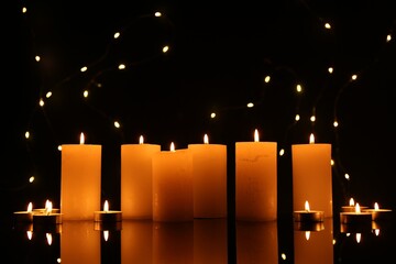 Many burning candles on mirror surface in darkness