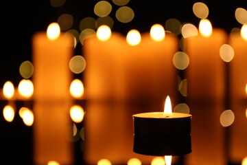 Burning candles on mirror surface in darkness, closeup. Bokeh effect
