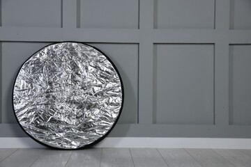 Professional reflector on floor near grey wall, space for text. Photo studio equipment