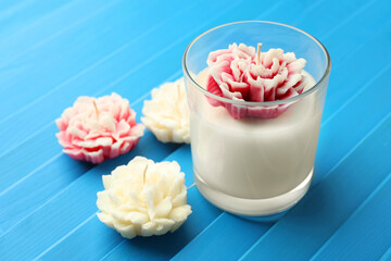 Beautiful flower shaped candles on blue wooden background, closeup