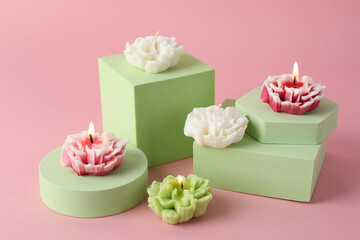 Beautiful burning flower shaped candles on pink background