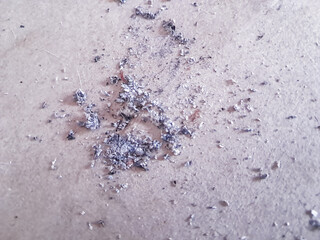 Close-up photograph captures a scattering of cigarette ash on a pale surface, possibly skin. The ash appears as a mix of gray, black, and white particles, with a grainy texture that contrasts wit