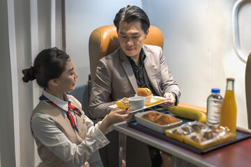 Female flight attendant serving meal to businessman on plane