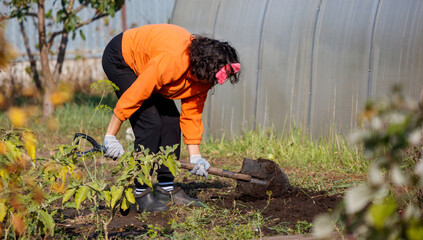 A woman in an orange shirt is digging a hole in the dirt