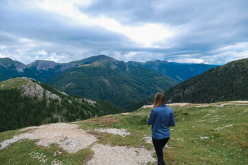 Naklejka premium A woman gazes at the stunning, lush panorama of the Nocky Mountains in Carinthia, Austria. Overlooking the vast, green hills under a cloudy sky, enjoying the scenic view and fresh air