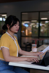 Young Asian woman reviewing documents and taking notes while studying with a tablet in an outdoor university study area