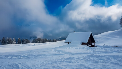 Wooden cabin sits nestled under a heavy blanket of snow in ski resort Nassfeld, Austria, with a...