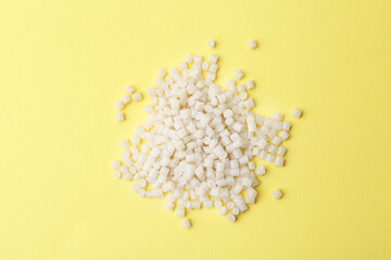 Pile of plastic granules on yellow background, top view