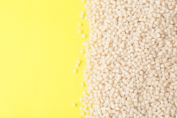 Pile of plastic granules on yellow background, top view. Space for text
