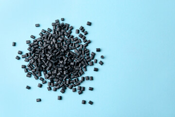 Pile of black plastic granules on light blue background, top view. Space for text