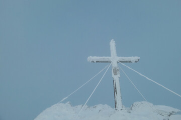 Summit cross, encased in frost and snow, stands firmly planted atop the peak of Moschkogel...