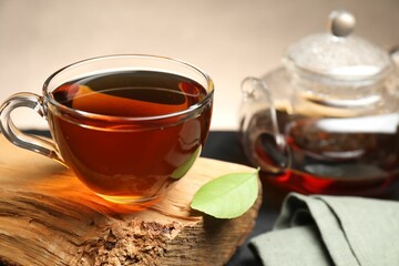 Aromatic black tea in cup and green leaf on table, closeup