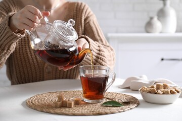 Woman pouring hot black tea into cup at white table, closeup