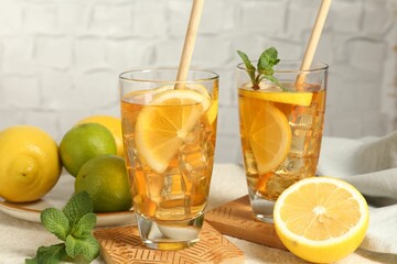 Refreshing iced tea with drinking straws, mint, lemon and lime on light table against grey background, closeup