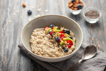 Oatmeal porridge with fruit and berries in bowl on the table. Homemade healthy breakfast cereal with strawberry, kiwi fruits, blueberry and almond